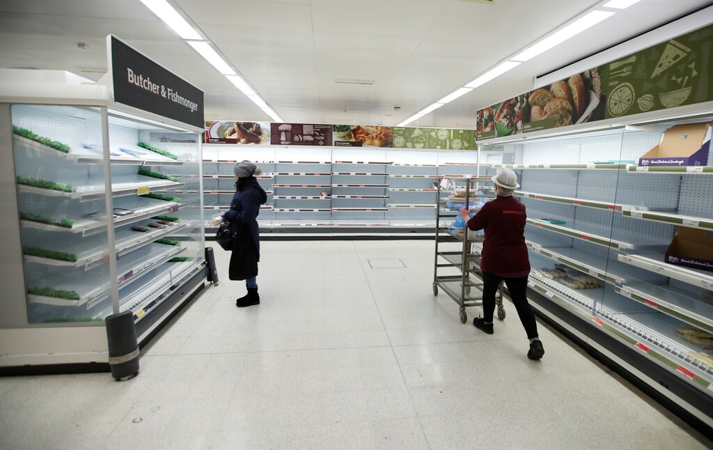 A Sainsbury's worker walks past a customer next to empty shelves at a Sainsbury's store in Harpenden as the spread of the coronavirus disease (COVID-19) continues, in Harpenden, Britain, March 18, 2020