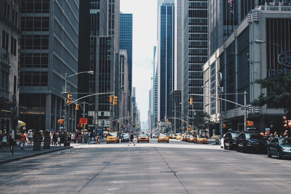 Photo taken of New York City, with cars and people crossing the street.
