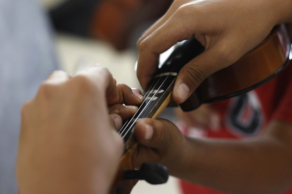 A student helps another student place fingers on the fingerboard of a violin during music lessons at their school in Ciudad Juarez, October 14, 2010. In one of the world's deadliest cities, where drug gangs murder a dozen people a day, a former heroin addict is changing lives with violins and trumpets rather than assault rifles. Alma Rosa Gonzalez is helping poor children learn classical music and give them an outlet that might stop them falling prey to the gangsters who are terrorizing this city of about 1.5 million on the Texas border. Picture taken October 14, 2010. To match feature MEXICO-DRUGS/ORCHESTRA REUTERS/Tomas Bravo (MEXICO - Tags: SOCIETY CIVIL UNREST EDUCATION) - RTXVH2S