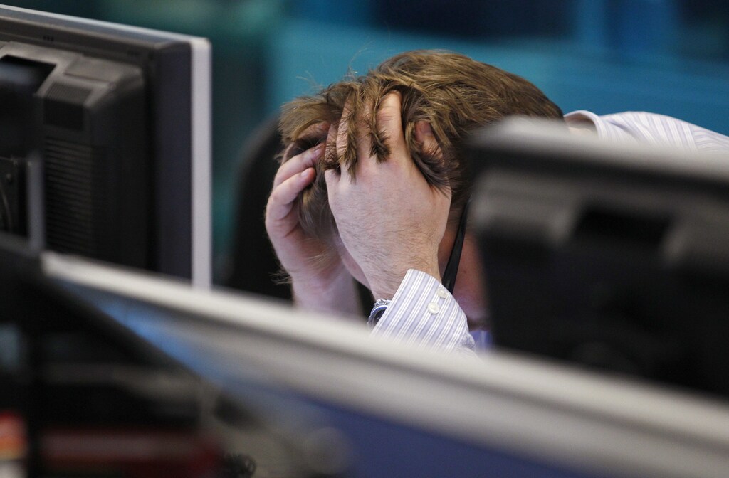 A worker on IG Index's trading floor holds his head in his hands as markets tumble globally.