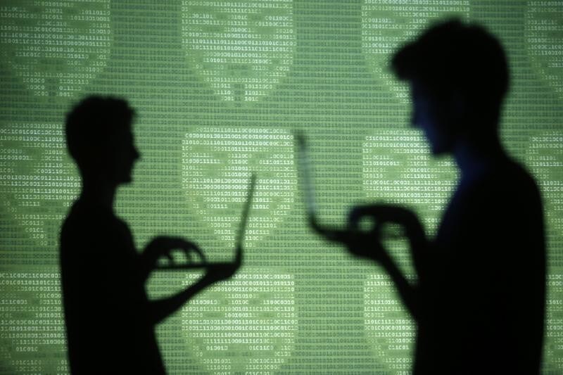People are silhouetted as they pose with laptops in front of a screen projected with 'Guy Fawkes' aka 'Anonymus' masks and binary code, in this picture illustration taken in Zenica October 29, 2014.