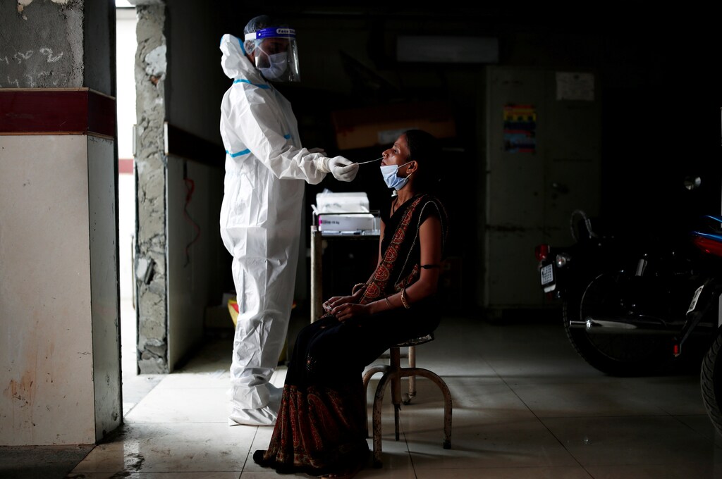 image of a medical health worker in personal protective equipment collecting a sample from a woman using a swab, at a local health centre to conduct tests for COVID19