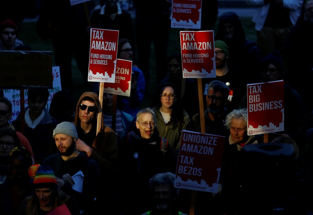 People cheer as they hold "Tax Amazon" signs during a protest in front of the Amazon Spheres to demand that the city of Seattle tax the largest corporations to help fund affordable housing, according to organizers, in Seattle, Washington, U.S., April 10, 2018