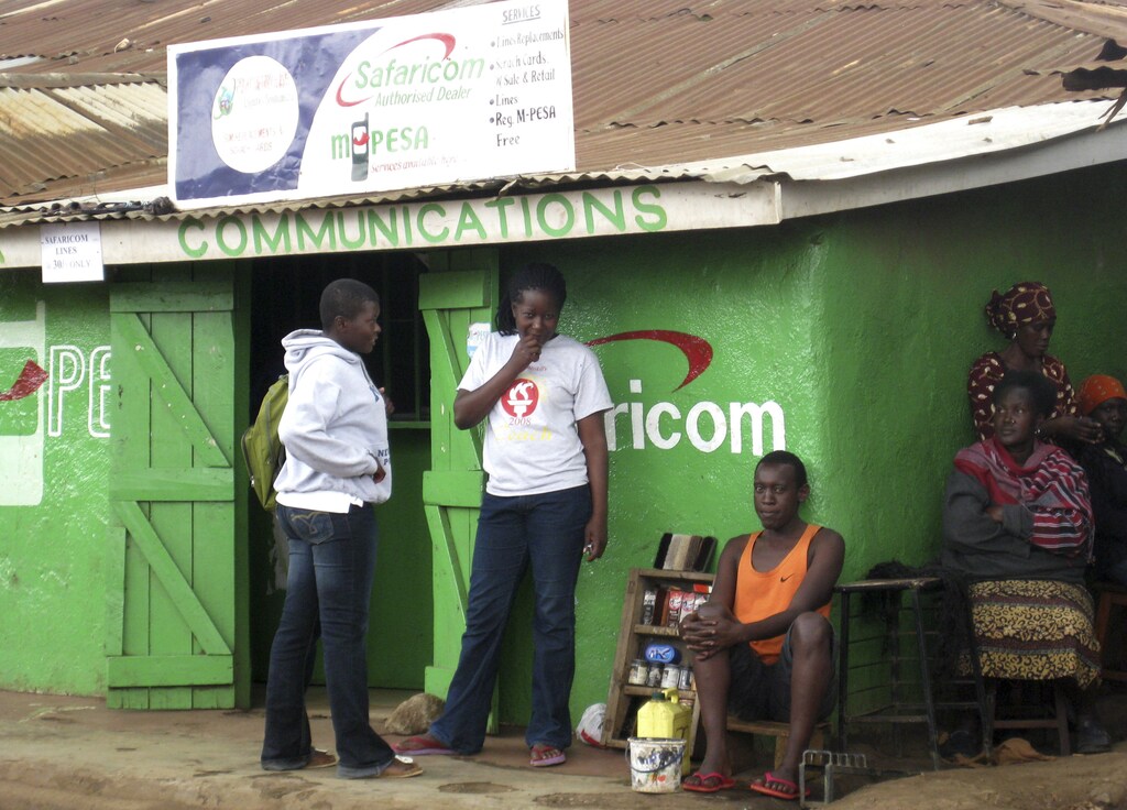 Residents sit outside a Safaricom retail stall in Nairobi's Kibera slum