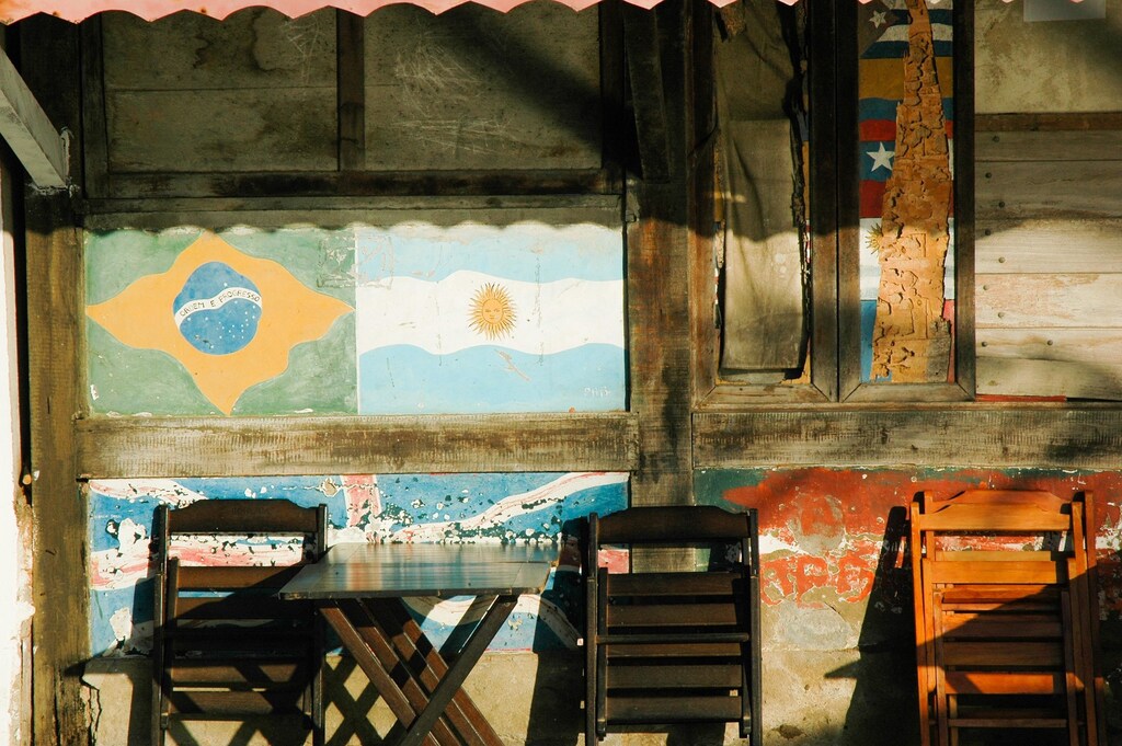 Folded wooden chairs leaning against wall paintings of Latin American flags.
