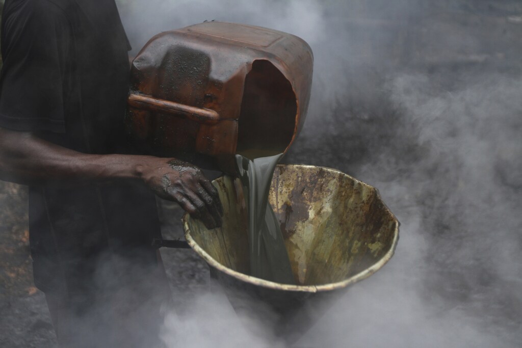 A man pours crude oil into a funnel enveloped by steam at an illegal oil refinery site near river Nun in Nigeria's oil state of Bayelsa November 25, 2012. Thousands of people in Nigeria engage in a practice known locally as 'oil bunkering' - hacking into pipelines to steal crude then refining it or selling it abroad. The practice, which leaves oil spewing from pipelines for miles around, managed to lift around a fifth of Nigeria's two million barrel a day production last year according to the finance ministry. Picture taken November 25, 2012. REUTERS/Akintunde Akinleye (NIGERIA - Tags: BUSINESS ENVIRONMENT SOCIETY INDUSTRIAL ENERGY) - GM1E91F187701