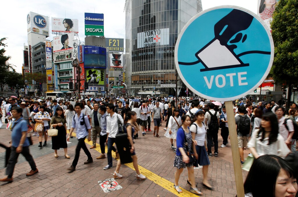 A member of the Students Emergency Action for Liberal Democracy (SEALDs) holds a placard calling on youths to vote in the July 10 upper house election, in front of a busy crossing in Shibuya district in Tokyo, Japan June 26, 2016. Picture taken June 26, 2016. REUTERS/Toru Hanai - RTX2J58J
