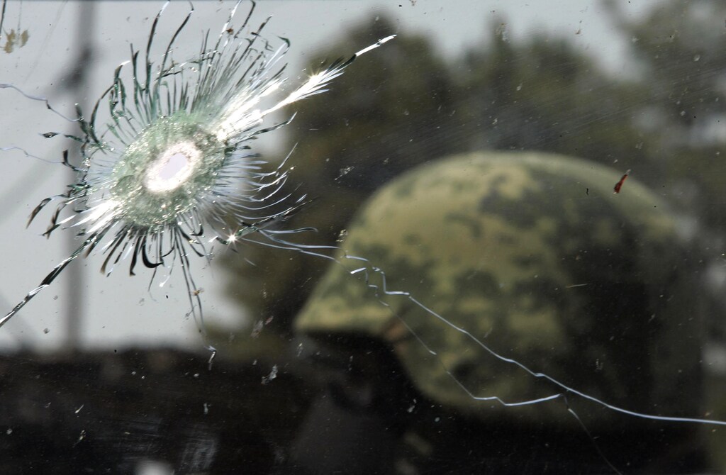 A soldier stands near the bullet-riddled window of a confiscated car in Tuxtepec March 24, 2010. Six people, five innocent bystanders and one hitman were killed after gunmen assaulted a motorcycle repair shop and then confronted an army patrol. No arrests have been reported but officials seized a cache of weapons including AR-15 automatic rifles, a grenade launcher and copies of police uniforms, police said