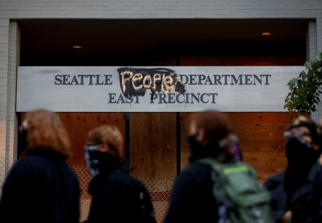 People stand in front of the Seattle Police Department's East Precinct sign, spray painted to replace "police" with "people" as the protesters established what they call an autonomous zone while continuing to demonstrate against racial inequality and call for defunding of Seattle police, in Seattle, Washington, U.S. June 9, 2020. Picture taken June 9, 2020. REUTERS/Lindsey Wasson TPX IMAGES OF THE DAY - RC276H9WJ22I