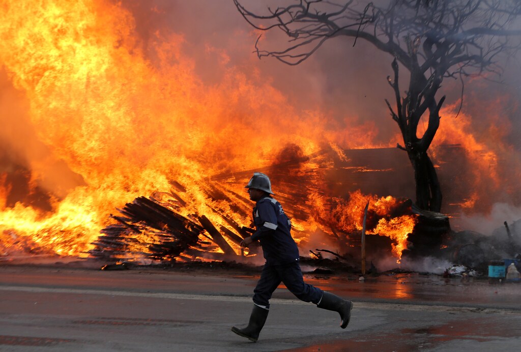 A firefighter runs past a burning tree and wooden packaging material after a fire broke out at a wood store in Ahmedabad, India, March 24, 2019. REUTERS/Amit Dave - RC128C1E4710