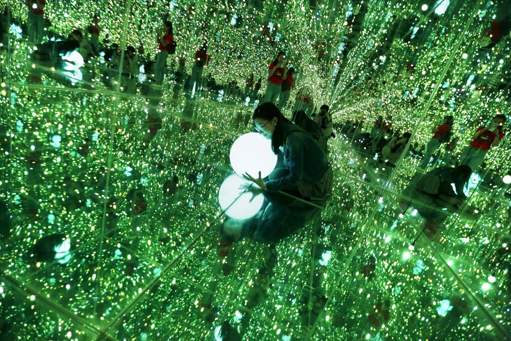 A visitor holding a light poses for a photograph in an optical illusion installation at the Imagine Your Museum of Art exhibition in Beijing.
