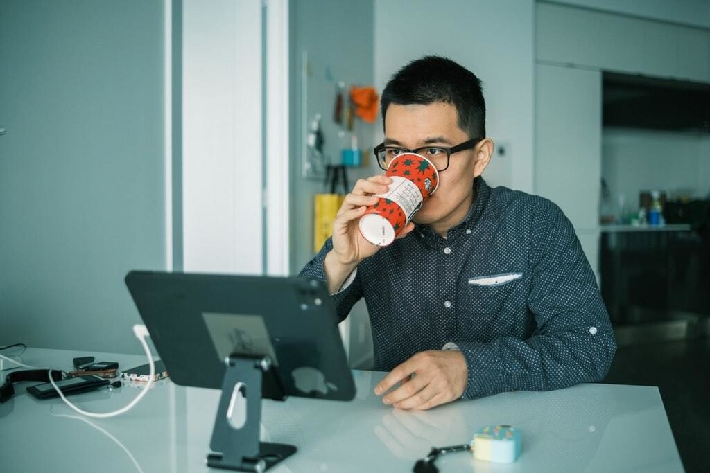Man sits on computer at home drinking coffee.