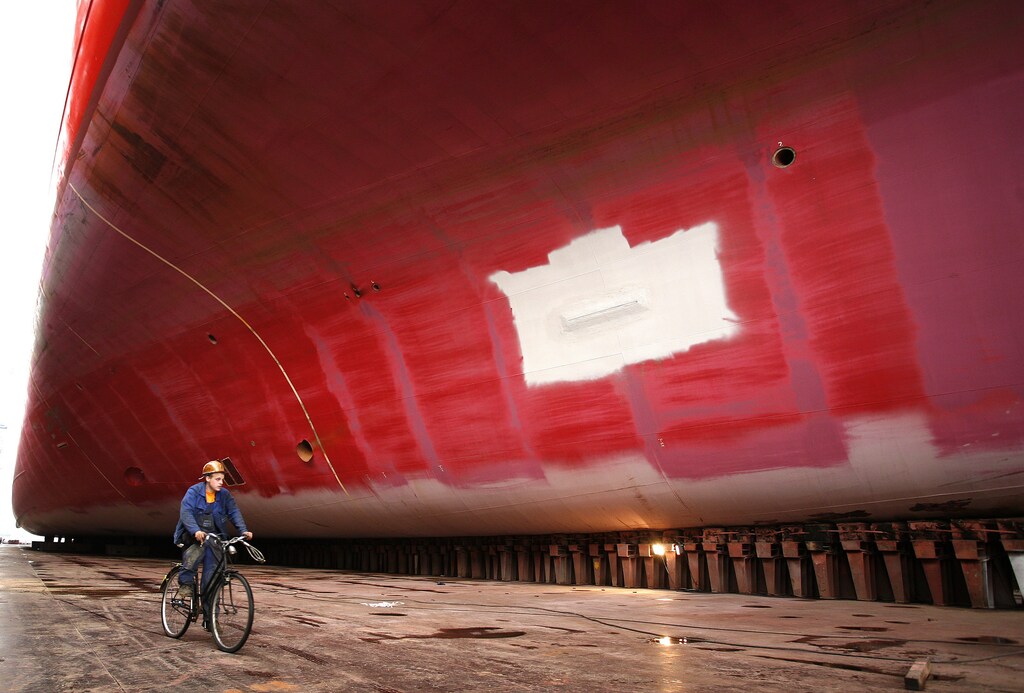 A worker rides his bicycle beside a container ship which is being prepared for painting work in a dry-dock at Blohm + Voss shipyard in Hamburg August 13, 2007.