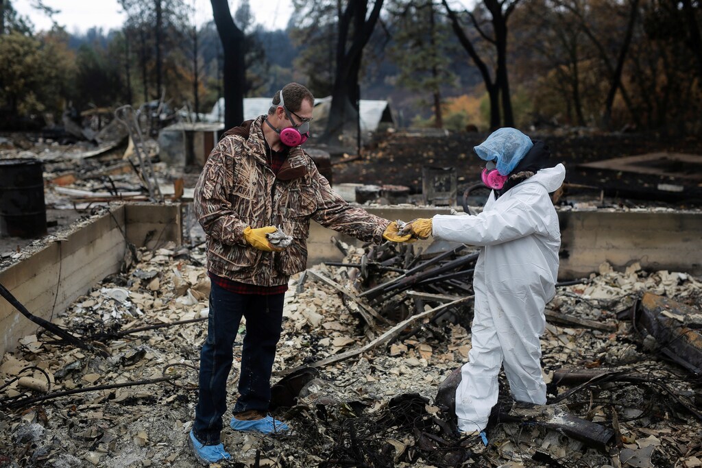 Vanthy Bizzle hands some small religious figurines to her husband Brett Bizzle in the remains of their home after returning for the first time since the Camp Fire forced them to evacuate in Paradise, California, U.S. November 22, 2018. REUTERS/Elijah Nouvelage - RC1C3BA983B0