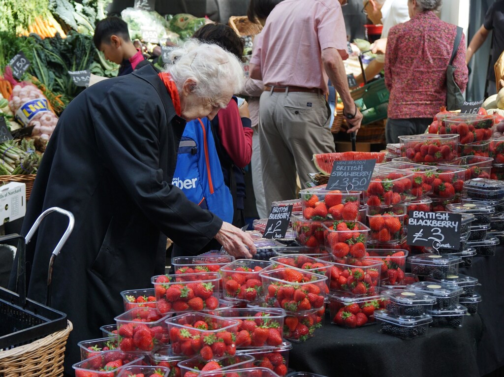 Person in a black jacket looking at plastic containers of fruit.