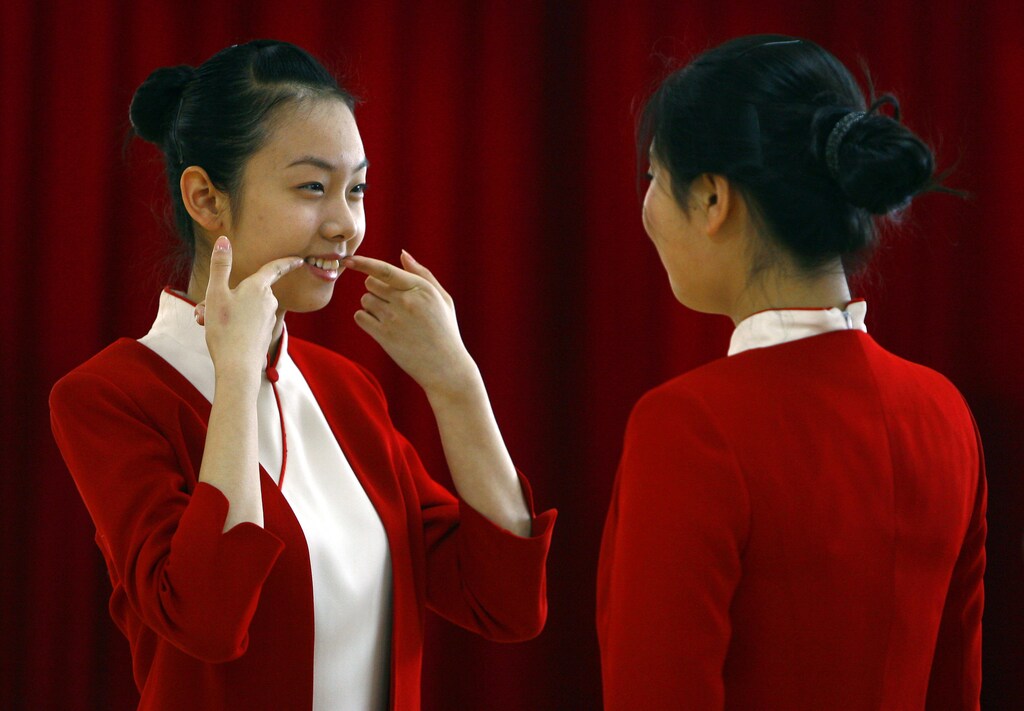 A student shows another how to smile during an etiquette training class at a vocational school in Beijing January 7, 2008. A small group of vocational students, mostly between the ages of 16 and 18, are going through physical conditioning as well as professional training for dressing and etiquette in order to be stewards for the service industry, but a select few will become stewards for medal ceremonies during the 2008 Beijing Olympics. REUTERS/David Gray (CHINA) - RTX5ATW