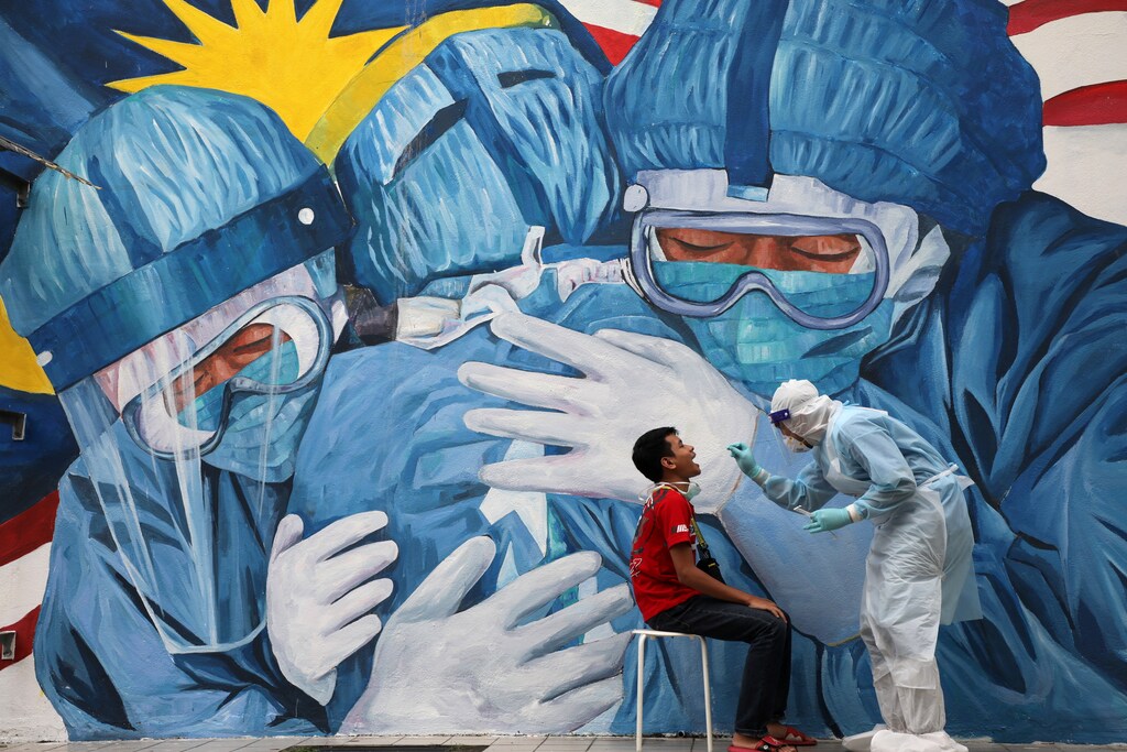 A doctor collects a swab sample from a man to be tested for the coronavirus disease against a mural depicting solidarity among healthcare workers.