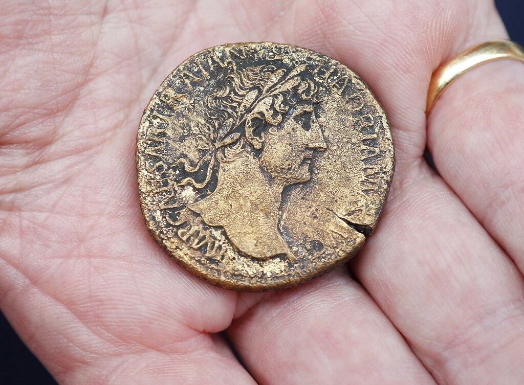 An archaeologist displays Roman Sestertius brass coin from around AD 30 with an image of the Emperor Hadrian which was dug out from the Crossrail site next to Liverpool Street Station in the City of London, August 7, 2013. The dig is on the site of the future ticket hall for the Crossrail station at Liverpool Street. Archaeologists have a window of time to dig through parts of London's first municipal graveyard from the 16 and 17th century; and through to the Roman ruins beneath; before the site is handed back to contractors building the ticket hall for the Crossrail station. REUTERS/Andrew Winning (BRITAIN - Tags: ENVIRONMENT SOCIETY) - GM1E98801FQ01