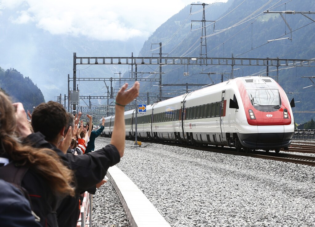 Guests waves at a train that has crossed the tunnel during the opening ceremony of the NEAT Gotthard Base Tunnel, the world's longest and deepest rail tunnel, near the town of Erstfeld, Switzerland June 1, 2016. The 57.1-km (35.5 mile)-long Gotthard Base Tunnel, 17 years under construction and designed to last a century, is part of a 23 billion Swiss franc (23.1 billion USD) infrastructure project to speed passengers and cargo by rail below the Alps, as much as 2.3 km (1.7 miles) under the mountain chain, that divides Europe's north and south. REUTERS/Arnd Wiegmann - RTX2F4E5