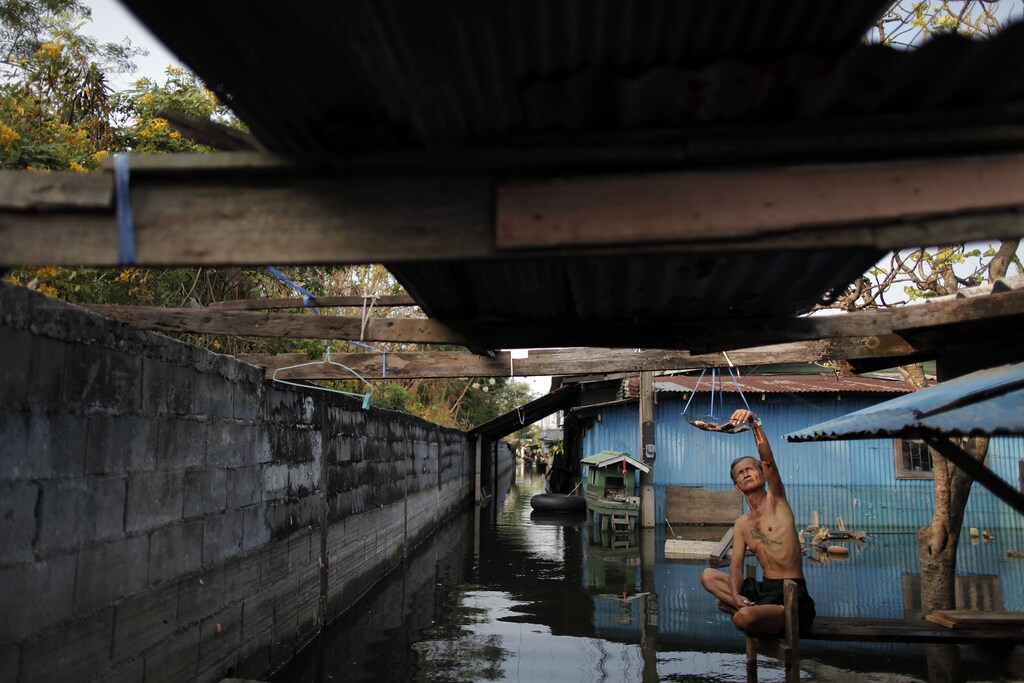 An elderly man checks dried fish outside his flooded home in a slum just outside Bangkok