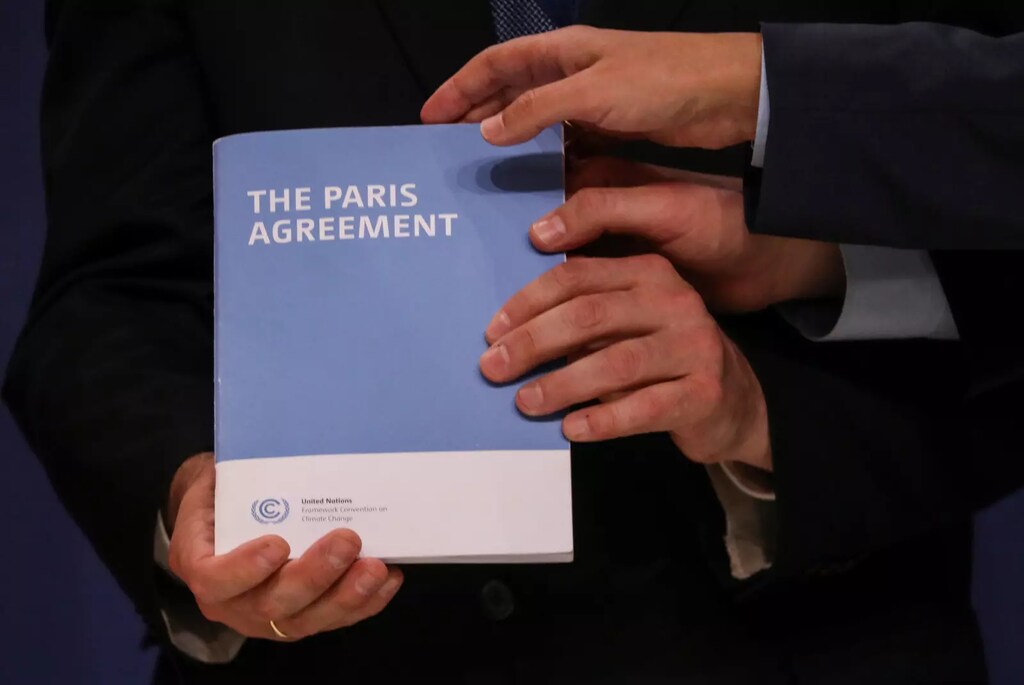 Varias manos sostienen una copia del Acuerdo de París, el plan global para mantener el aumento de la temperatura por debajo de los 2 °C con respecto a los niveles preindustriales.