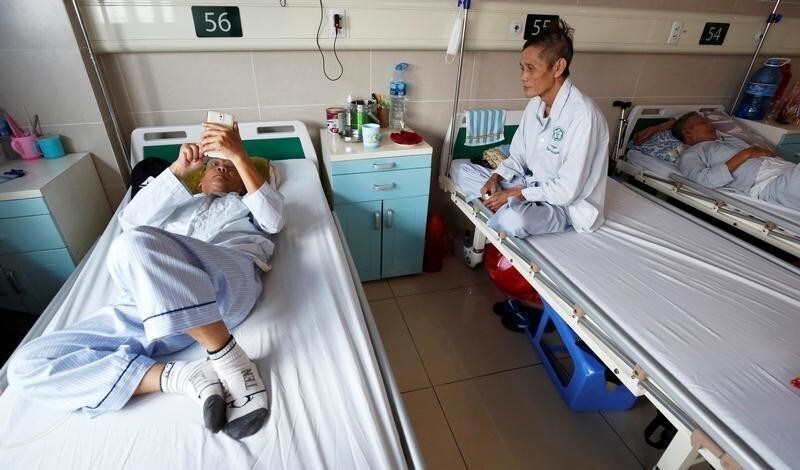 75 year old retired engineer Tran Ngoc Tran surfs internet as 63 years old retired soldier Nguyen Hong Phong sits on a bed, at a hospital in Hanoi, Vietnam October 9, 2018.