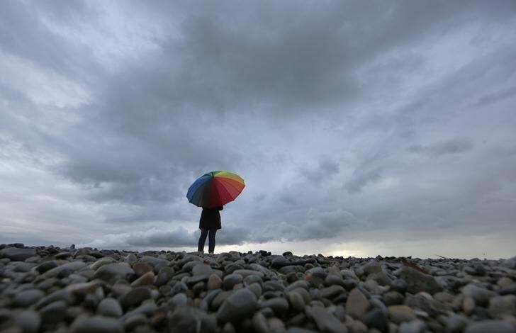 A woman protects herself under an umbrella on the beach in Nice while heavy rain and storm hit southeastern France November 15, 2014. REUTERS/Eric Gaillard (FRANCE - Tags: ENVIRONMENT)