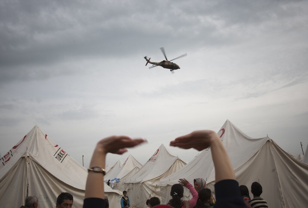 People wave at a military helicopter flying past at a stadium currently used as a relief shelter campsite for earthquake victims in Ercis October 26, 2011. REUTERS/Morteza Nikoubazl (TURKEY - Tags: DISASTER ENVIRONMENT TPX IMAGES OF THE DAY TRANSPORT) - GM1E7AR0FMT01