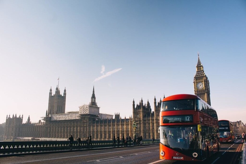 A red London bus is seen on London Bridge, in front of big ben and the houses of Parliament.
