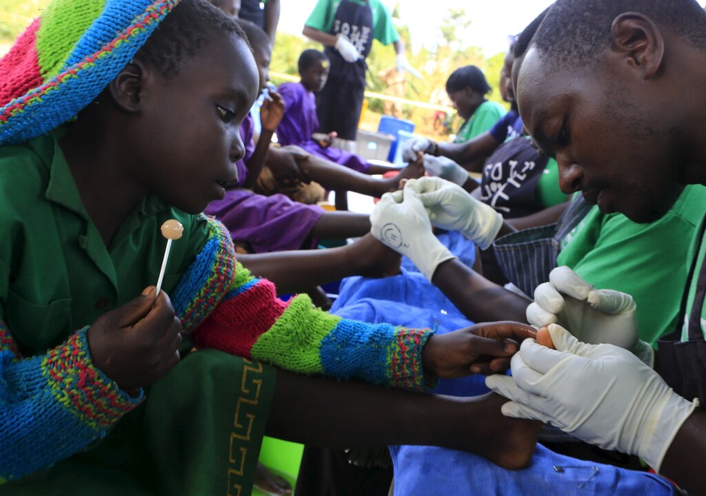 A schoolgirl sits with her schoolmates and sucks a lollipop to soothe her as her foot is examined to remove jiggers from it in Kalebera village, Jinja district, eastern Uganda August 6, 2015.