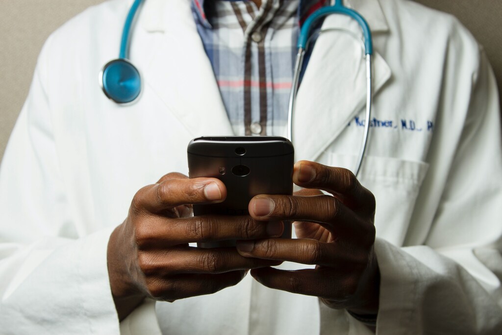 Man in white coat holding a mobile device: From medicine to industry, no-code platforms can speed up digitalization across a range of sectors.