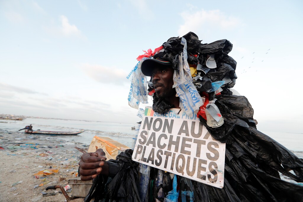Modou Fall, 43, head of Senegal Propre ("Clean Senegal") Association who is covered with plastic cups and bags to raise awareness of the damage on the environment caused by plastic waste talks to residents as he walks in a fishermen port on the outskirts of Dakar, Senegal July 26, 2019. The placard reads: "No to a plastic bags." Picture taken July 26, 2019. REUTERS/Zohra Bensemra - RC1299E33270