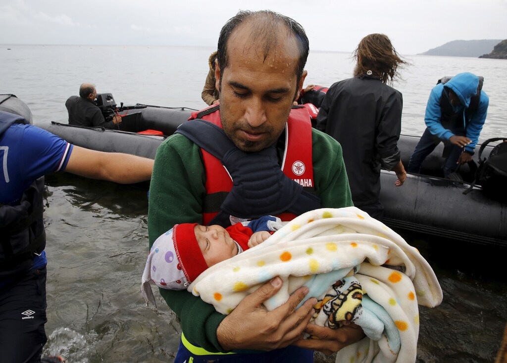 A Syrian refugee carries his baby child off an overcrowded dinghy after crossing part of the Aegean Sea from Turkey to the Greek island of Lesbos September 23, 2015.
