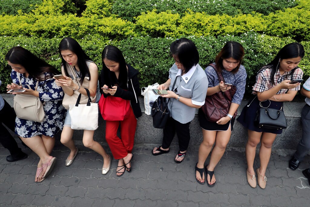 Women use their mobile phones while waiting for a bus at rush hour in Bangkok, Thailand October 4, 2018. REUTERS/Jorge Silva - RC150B3A10D0