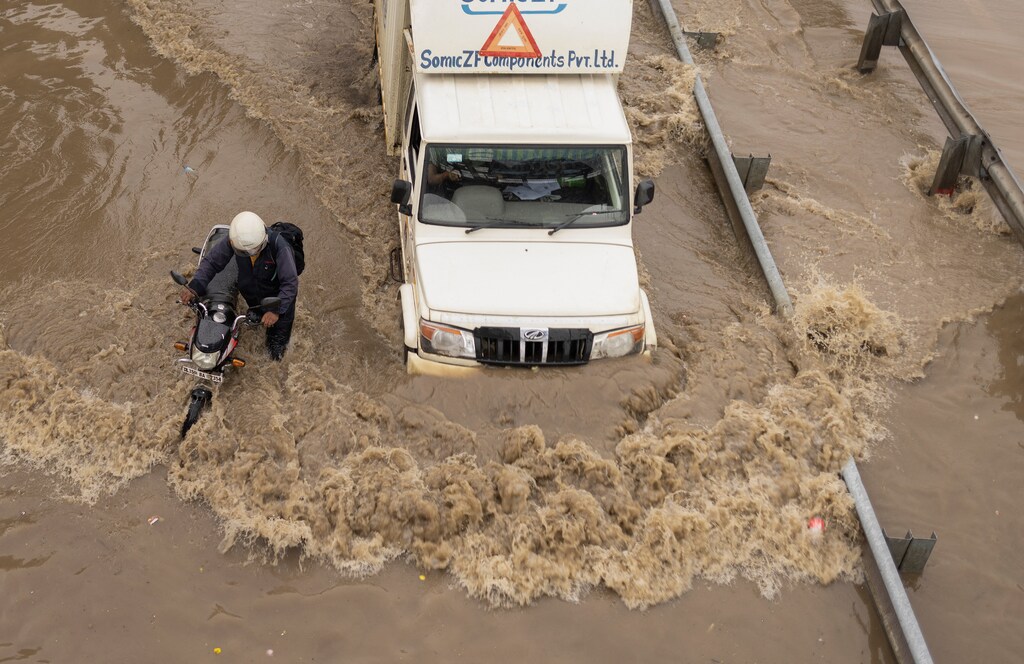A man pushes his stalled motorbike on a flooded street as a truck drives past after heavy rains in Gurugram, on the outskirts of New Delhi, India, 23 September 2022.