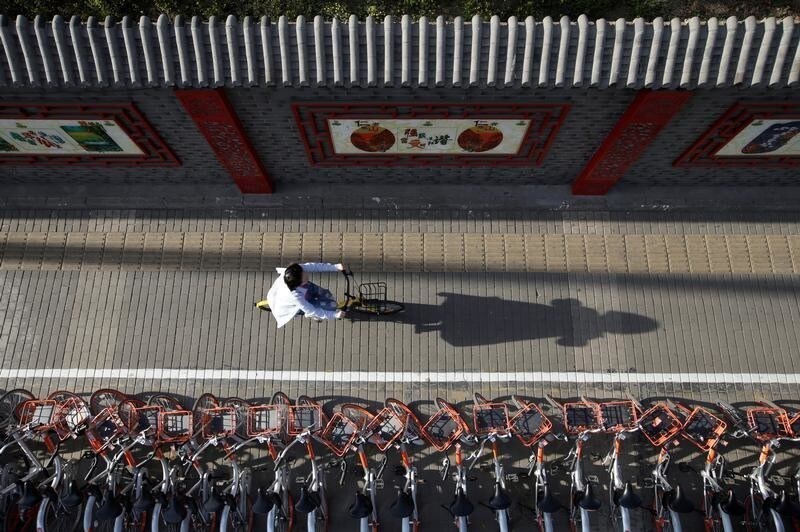 A woman rides an Ofo's shared bike past Mobike's shared bikes in Beijing's central business area, China April 21, 2017. Picture taken April 21, 2017. REUTERS/Jason Lee TPX IMAGES OF THE DAY - RC139EF1A570