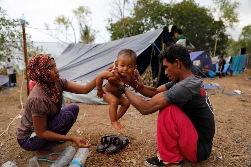 A couple of villagers worried about earthquake aftershock and tsunami wash their son at an empty resort atop a hill in Senggigi beach, Lombok Island, Indonesia, August 8, 2018.