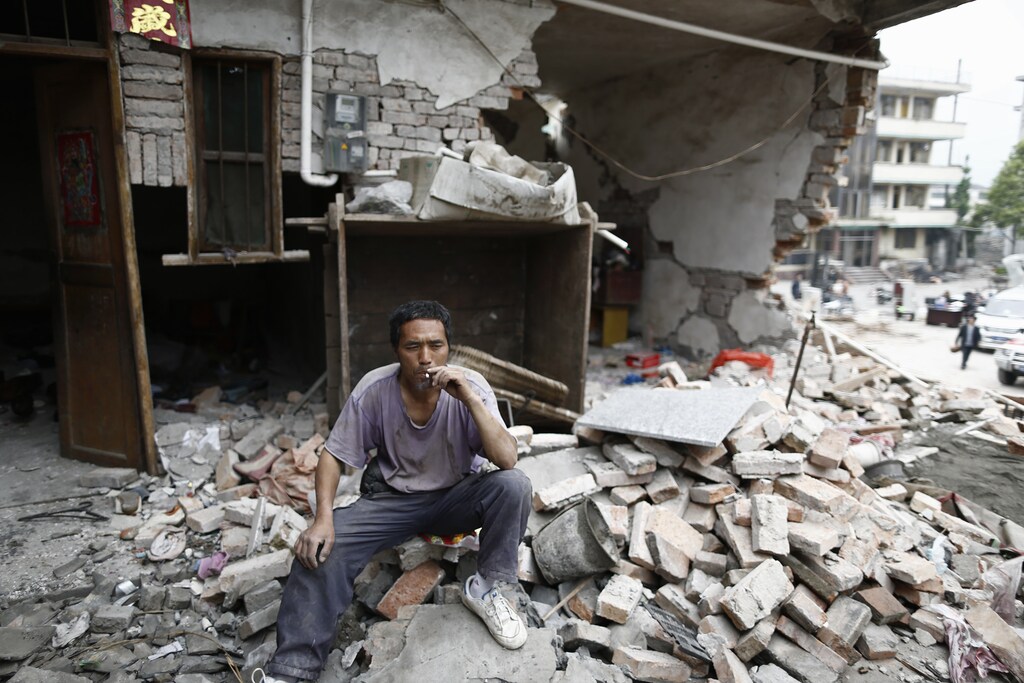 A man smokes a cigarette in front of a damaged house after an earthquake in China.