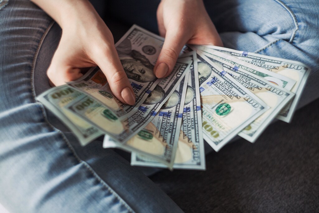 Close-up on hands holding 100 dollar US bank notes all fanned out. Here are some of the human impacts of the cost of living crisis - and what countries are doing to help.