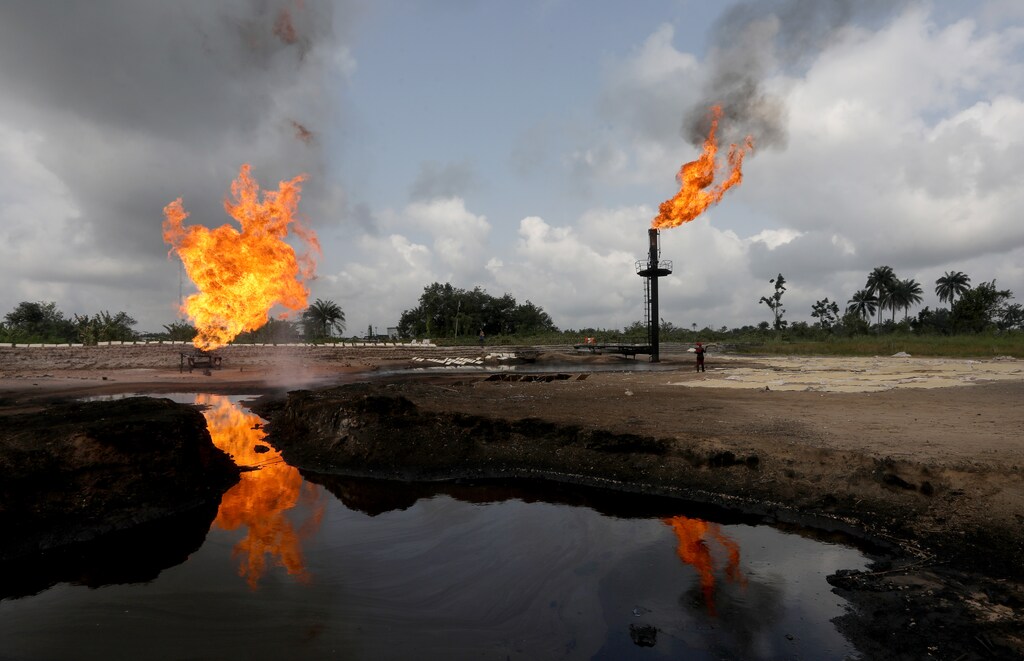 A reflection of two gas flaring furnaces is seen in the pool of oil-smeared water at a flow station in Ughelli, Delta State, Nigeria September 17, 2020. Picture taken September 17, 2020