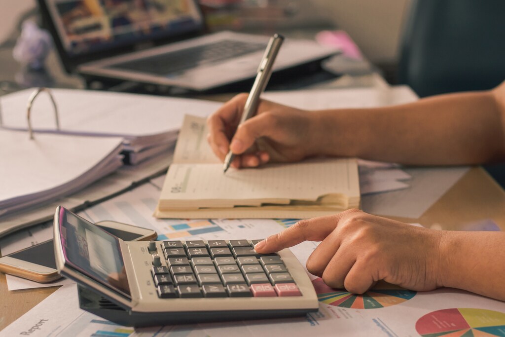 Man hand using a financial calculator with writing make note and Financial data analyzing on desk at home
