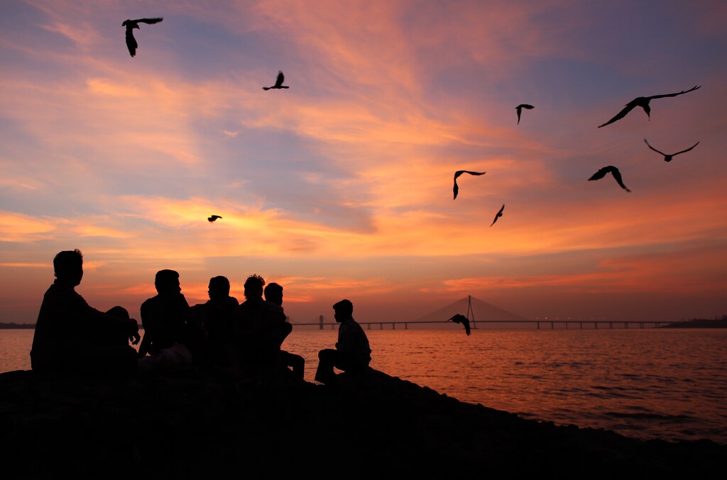 A group of men are silhouetted as they sit on a sea wall along the Arabian Sea in Mumbai at sunset October 24, 2013.