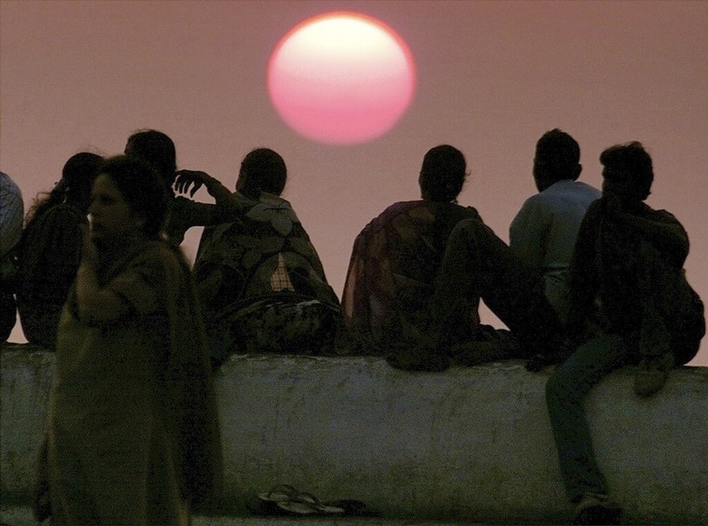A group of people sit on a sea-wall watching the sunset over the Arabian Sea in Bombay in this March 3, 2001 file photo. Dumping iron dust in the seas or placing smoke and mirrors in the sky to dim the sun could help a world struggling to curb global warming, according to backers of extreme technologies. To match feature CLIMATE/GEOENGINEERING REUTERS/Stringer/Files