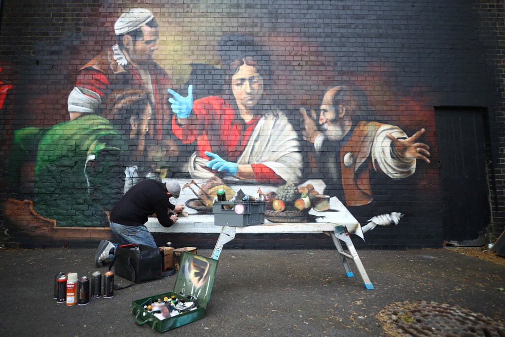 Artist Lionel Stanhope paints a mural in Ladywell depicting the Supper at Emmaus by Caravaggio with added protective gloves, following the outbreak of the coronavirus disease (COVID-19), London, Britain, May 5, 2020. REUTERS/Hannah McKay - RC2AIG94UANW
