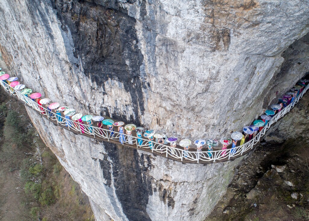 Women wearing cheongsam pose for pictures on a walkway along a cliff during an event in Chongqing Municipality, China March 26, 2017. Picture taken March 26, 2017. REUTERS/Stringer ATTENTION EDITORS - THIS IMAGE WAS PROVIDED BY A THIRD PARTY. EDITORIAL USE ONLY. CHINA OUT. NO COMMERCIAL OR EDITORIAL SALES IN CHINA. TPX IMAGES OF THE DAY - RTX32UP8