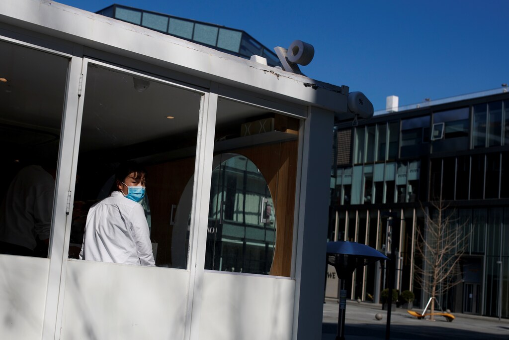 A sales woman wearing a face mask looks out of a coffee shop in an upmarket shopping district in Beijing as the country is hit by an outbreak of the novel coronavirus, China, March 4, 2020. REUTERS/Thomas Peter - RC2WCF9882GE