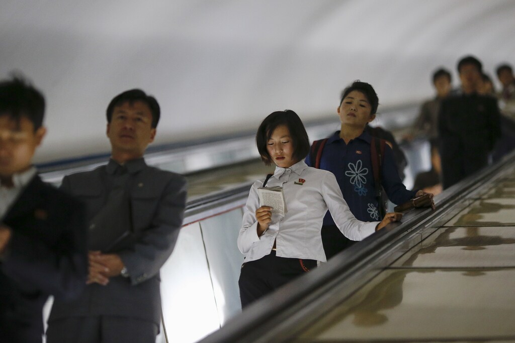 A woman reads a book as commuters make their way through a subway station in Pyongyang, North Korea October 9, 2015. Picture taken October 9, 2015. To match Insight NORTHKOREA-CHANGE/ REUTERS/Damir Sagolj - GF20000035870