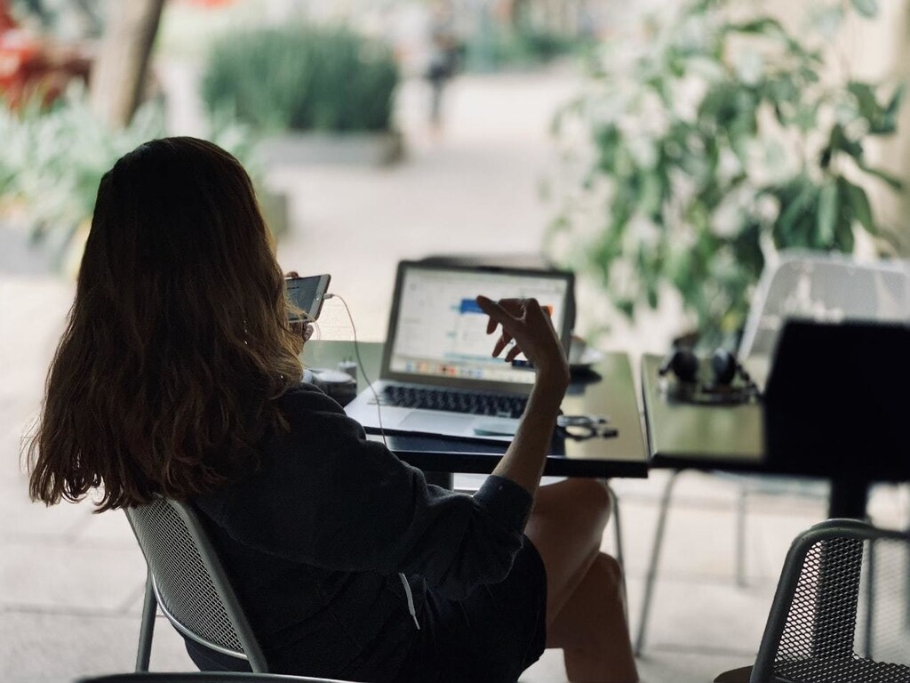 Lady sits at laptop, watching a video on her phone whilst working at home. A prime example of the recent rapid digitisation following COVID-19.