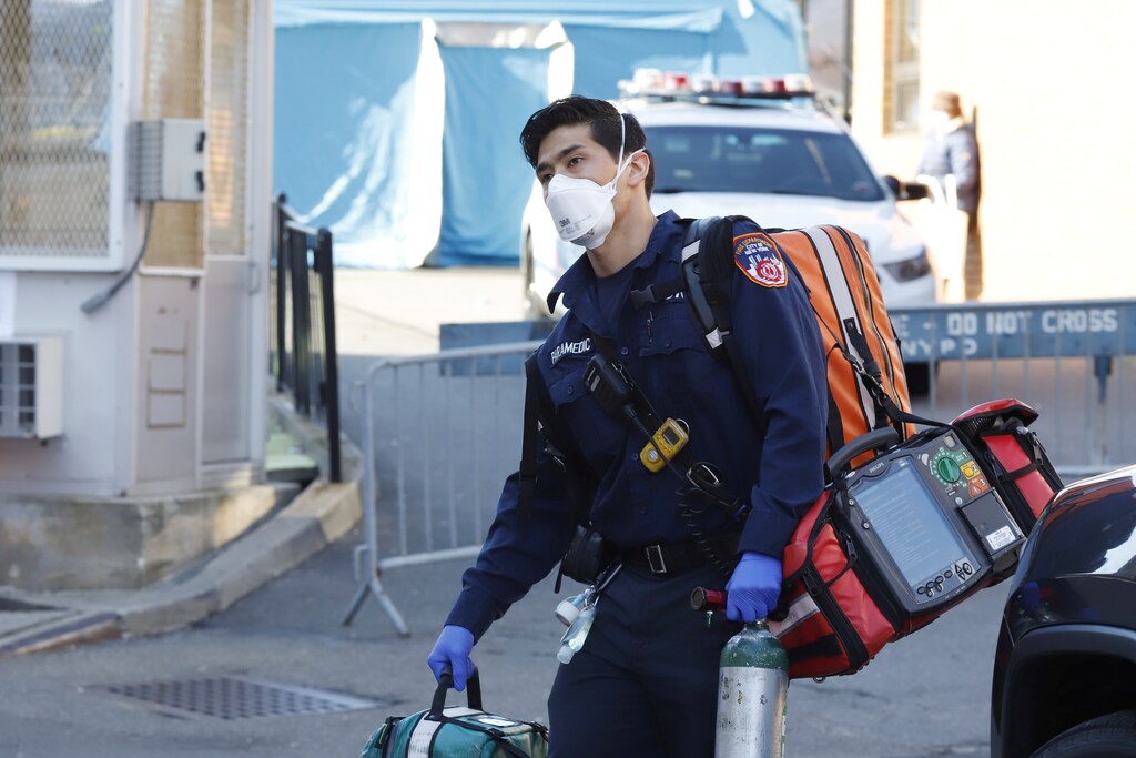 An emergency medical technician carries equipment near where people are waiting to be tested for coronavirus disease (COVID-19) outside Elmhurst Hospital Center in the Queens borough of New York City, U.S., March 26, 2020. REUTERS/Stefan Jeremiah - RC2RRF91IRAX