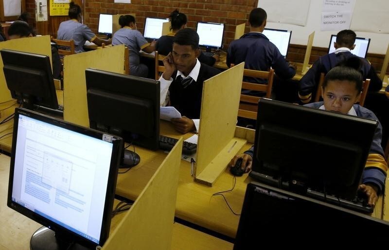 Students use computers to study at Elswood Secondary School in Cape Town November 7, 2013. Even the metal grills welded into its walls did not deter burglars from ripping out the copper cables that delivered Internet to the students of this tough neighbourhood. But Elswood's pupils were saved by alternative technology - free wireless connection via unused TV spectrum known as white space. It's being provided by a consortium including Google as part of a wider trial. Elsewhere in the country Microsoft is operating similar pilots. Both are racing to fine tune a technology that could ultimately bring cheap broadband to the entire continent. Picture taken November 7, 2013. To match Feature AFRICA-INTERNET/ REUTERS/Mike Hutchings (SOUTH AFRICA - Tags: EDUCATION BUSINESS SCIENCE TECHNOLOGY) - RTX157JS